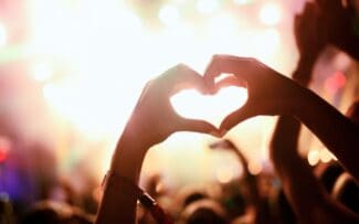 Two hands illuminated against the backdrop of a night festival in Fairfield, forming a heart shape symbol.